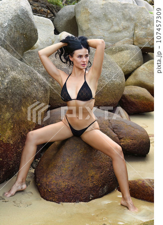 Slender sexy ukrainian 37 years old woman in black bikini sitting on the stones and holding her hair 107457309