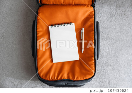 Travel Packing List For Vacation mockup. Travel Packing Checklist For Holiday Or Business Trip. Open empty notepad with pen in orange suitcase on bed at home Travel Packing List For Vacation mockup. Travel Packing Checklist For Holiday Or Business Trip. Open empty notepad with pen in orange suitcase on bed at home 107459624