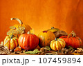 Colorful display of pumpkins, autumn leaves sitting in a row on woodentable, orange background 107459894