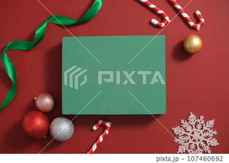 Top view of a green gift box displayed on red background with colorful baubles, candy canes, ribbon and snowflakes decorated. Blank space for display product 107460692