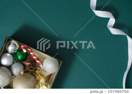 Christmas decoration composition on dark green background with a small gift box filled with beautiful baubles and silver ribbon. Creative background for advertising and space for design 107460700