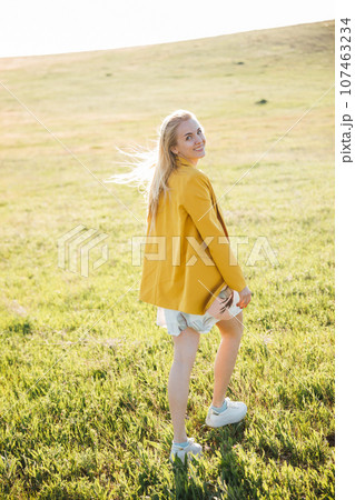 beautiful blonde in a yellow jacket in nature green glade 107463234