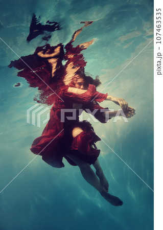 A woman in a red dress poses underwater as if she is flying 107463535