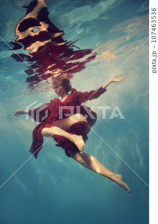 A woman in a red dress poses underwater as if she is flying 107463536