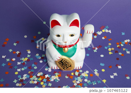 a white Maneki-neko plastic cat, on a confetti carpet 107465122