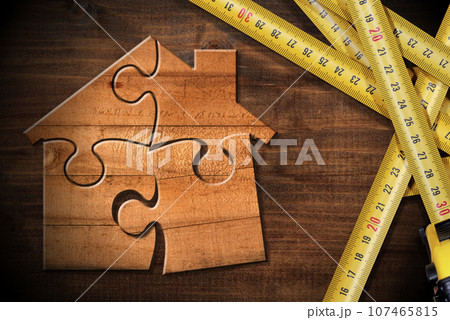 Tape Measures and a Wooden House made of Puzzle Pieces on Workbench 107465815