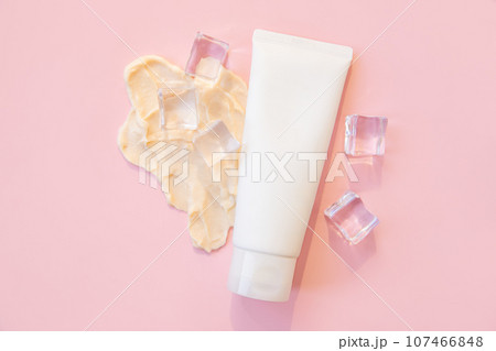cosmetic cream moisturizer in tube bottle, smeared thick cream and ice cubes on pink background. unbranded lotion, balsam, hand creme, toothpaste, container of cream, skin care. packaging mockup. 107466848