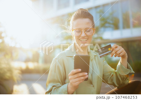 smiling woman worker in green blouse and eyeglasses using phone 107468253