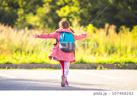 Rear view of little girl wearing backpack running with open arms after school on sunny parking Rear view of little girl wearing backpack running with open arms after school on sunny parking 107468282