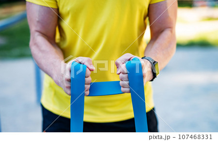 Man working out with resistance rubber bands in street, close up Man working out with resistance rubber bands in street, close up 107468331