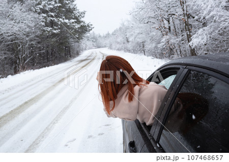 young beautiful red-haired woman looks out of the car window on the background of a snowy forest young beautiful red-haired woman looks out of the car window on the background of a snowy forest 107468657