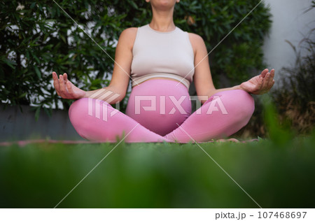 young beautiful pregnant woman meditates sitting on a yoga mat on a green lawn. relaxation and healthy lifestyle concept 107468697