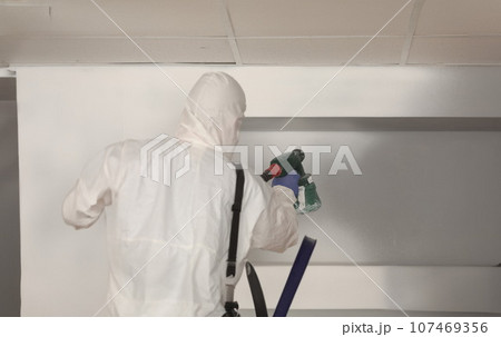 Worker paints wall white with spray gun 107469356