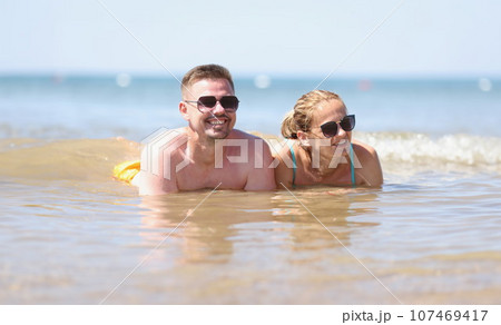 Happy couple in sunglasses lies on beach in sea Happy couple in sunglasses lies on beach in sea 107469417