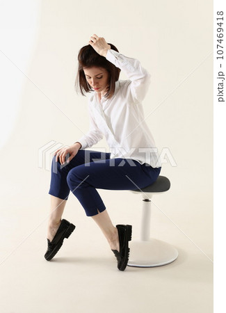 Woman in bad mood, bored and sad, sits on chair and puts hands on head Woman in bad mood, bored and sad, sits on chair and puts hands on head 107469418