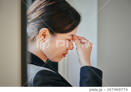 窓際に立ち眉間に手を当てる若い女性 107469774