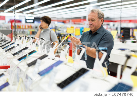 Elderly male customer looking for a deal on smart watches in big electronics store 107470740