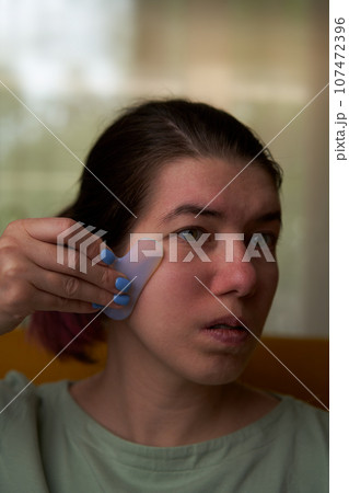Woman is massaging her face scraper gua sha. Woman is massaging her face scraper gua sha. 107472396