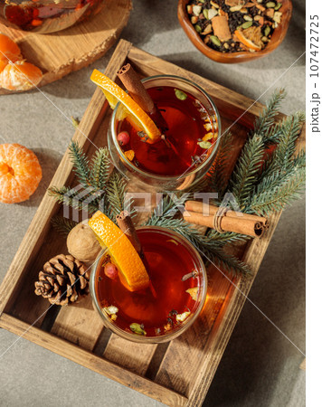 Spiced tea or mulled wine in glass cups with orange slices and cinnamon on a wooden tray. Top view, close-up. 107472725
