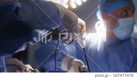 Adult male surgeon looks at monitor and operates patient Adult male surgeon looks at monitor and operates patient 107473476