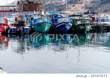 Reflection in the sea surface of white yachts parked in the port on the shore. Fragment of a ship on the water and the reflection of ships in the sea. motionless mirrored water of the sea Reflection in the sea surface of white yachts parked in the port on the shore. Fragment of a ship on the water and the reflection of ships in the sea. motionless mirrored water of the sea 107473571