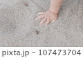 Baby enjoying putting his hands in sand at a beach. 107473704