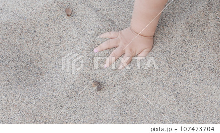 Baby enjoying putting his hands in sand at a beach. Baby enjoying putting his hands in sand at a beach. 107473704