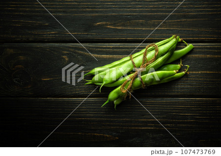 Beans in pods tied with a thread in a bunch on a wooden black table. Fresh beans after harvest are prepared for sale Beans in pods tied with a thread in a bunch on a wooden black table. Fresh beans after harvest are prepared for sale 107473769