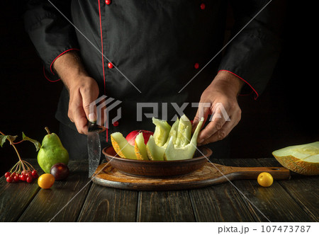 The cook puts fruit on a plate for serving for dessert. Fruit diet concept in hotel kitchen. Asian national cuisine The cook puts fruit on a plate for serving for dessert. Fruit diet concept in hotel kitchen. Asian national cuisine 107473787