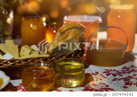 a jar of sweet honey on a table from a garden with apples in a bowl drips from a brush from a spoon a glass jar with cheese and roses and fresh bread with bright light beautiful decoration creative 107474142