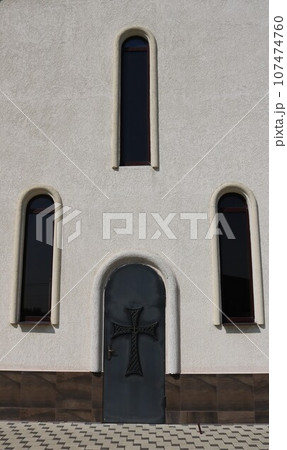 light wall of a religious building with arched narrow windows and an old door with a Christian cross, vertical image, fragment of the outside of the Armenian Orthodox Church as an exterior background light wall of a religious building with arched narrow windows and an old door with a Christian cross, vertical image, fragment of the outside of the Armenian Orthodox Church as an exterior background 107474760