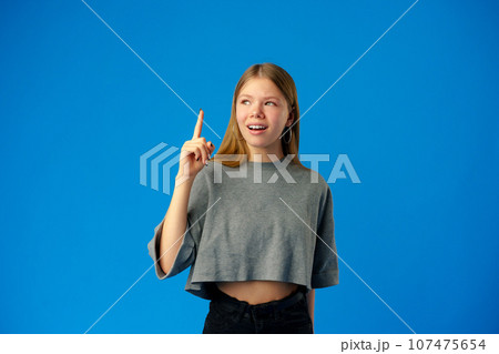 Young teenager girl pointing up with finger on blue background 107475654