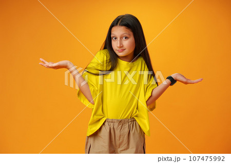 Puzzled teen girl don't know what to do on yellow background in studio Puzzled teen girl don't know what to do on yellow background in studio 107475992