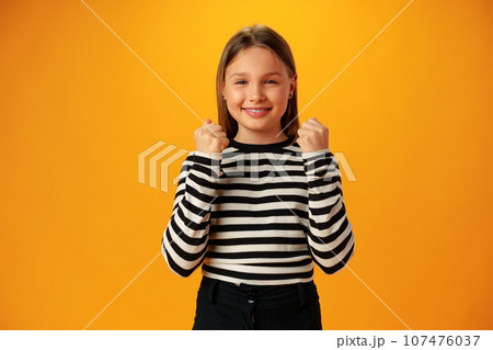 Portrait of a joyful happy teenage girl celebrating success on yellow background 107476037