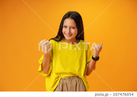 Portrait of a joyful happy teenage girl celebrating success on yellow background Portrait of a joyful happy teenage girl celebrating success on yellow background 107476054
