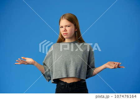 Puzzled teen girl don't know what to do on blue background in studio Puzzled teen girl don't know what to do on blue background in studio 107476164