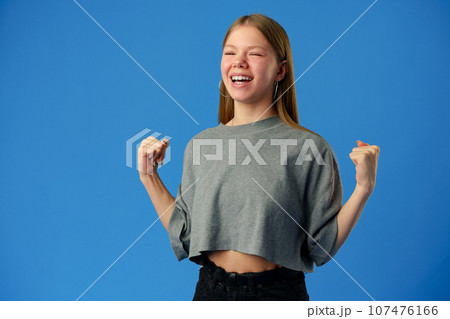 Portrait of a joyful happy teenage girl celebrating success on blue background Portrait of a joyful happy teenage girl celebrating success on blue background 107476166