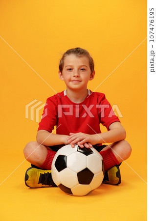 Teen boy soccer player with football ball against yellow background 107476195