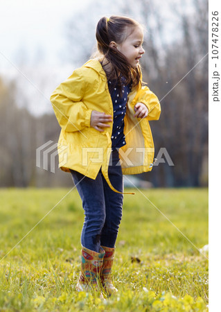 Joyful girl jumping up while standing in puddle on lawn, looking down with carefree expression, enjoying fall day. 107478226