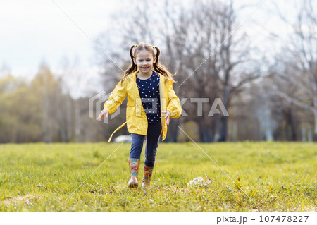 Loveable little girl looking down with smile and eyes full of carefree while strolling across lawn on autumn day. 107478227