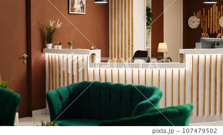 Stylish posh welcoming rustic resort lobby interior filled with green cozy luxurious chairs and sofa, waiting for visitors. Empty hotel reception desk ready for arriving guests Stylish posh welcoming rustic resort lobby interior filled with green cozy luxurious chairs and sofa, waiting for visitors. Empty hotel reception desk ready for arriving guests 107479502