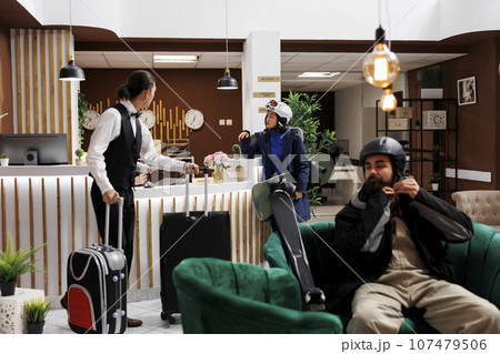 Arrival at modern hotel lobby, check-in, cozy lounge, luxury resort, winter gear, recreation, relaxation, exclusive holiday. Youthful tourists in lounge area awaiting accommodation. 107479506