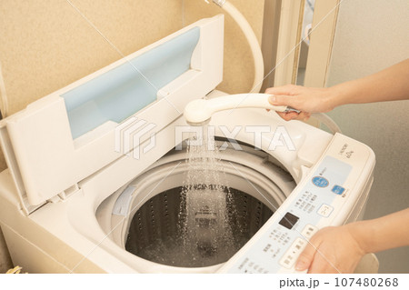 洗濯槽にシャワーでお湯を入れる女性の手元 107480268