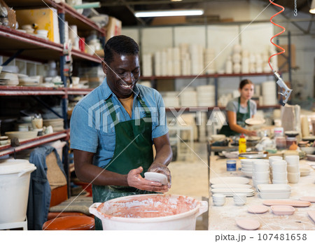 Cheerful man potter painting plates in workshop Cheerful man potter painting plates in workshop 107481658