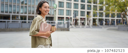 Stylish city girl with tablet, walking on street and drinking takeaway coffee, going to university or work 107482523