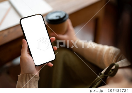 Close-up image of a woman using her smartphone while sitting in a coffee shop. Close-up image of a woman using her smartphone while sitting in a coffee shop. 107483724
