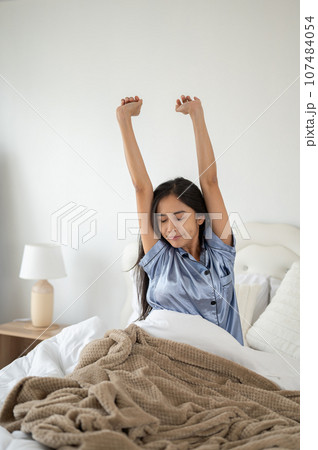 A relaxed and carefree Asian woman in pajamas is stretching her arms after waking up in the morning. 107484054