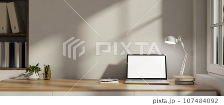 A laptop on a wooden desk against the white wall in a modern minimalist home office. A laptop on a wooden desk against the white wall in a modern minimalist home office. 107484092