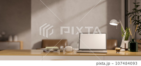 A wooden desk in a minimalist home office with a white-screen laptop mockup and accessories. A wooden desk in a minimalist home office with a white-screen laptop mockup and accessories. 107484093
