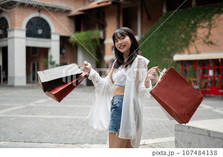 A pretty Asian woman is carrying her shopping bags and enjoying her shopping day in the city. 107484138